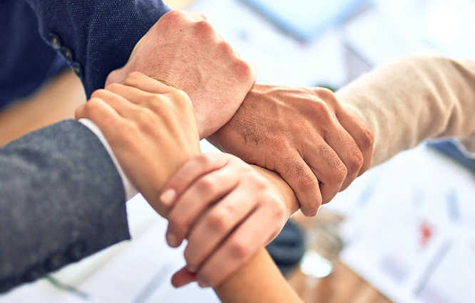 Vier Hände greifen an den Arm der nächsten Person, das Zusammenarbeit darstellt