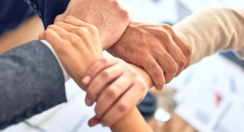 Vier Hände greifen an den Arm der nächsten Person, was kombinierte Zusammenarbeit darstellen soll