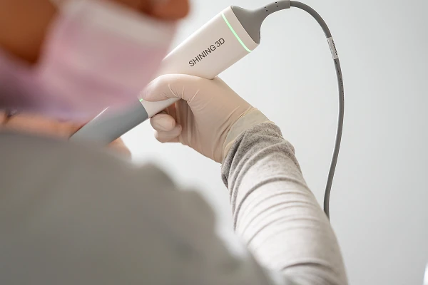 Hand im Untersuchungshandschuh hält einen Intraoralscanner für den digitalen Zahnabdruck.