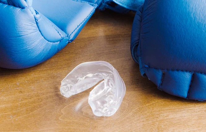 Transparenter Sportmundschutz auf einer Holzoberfläche zwischen zwei blauen Boxhandschuhen.